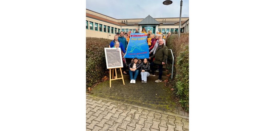 Mehrere Personen stehend vor einem Gebäude, eine Fahne haltend