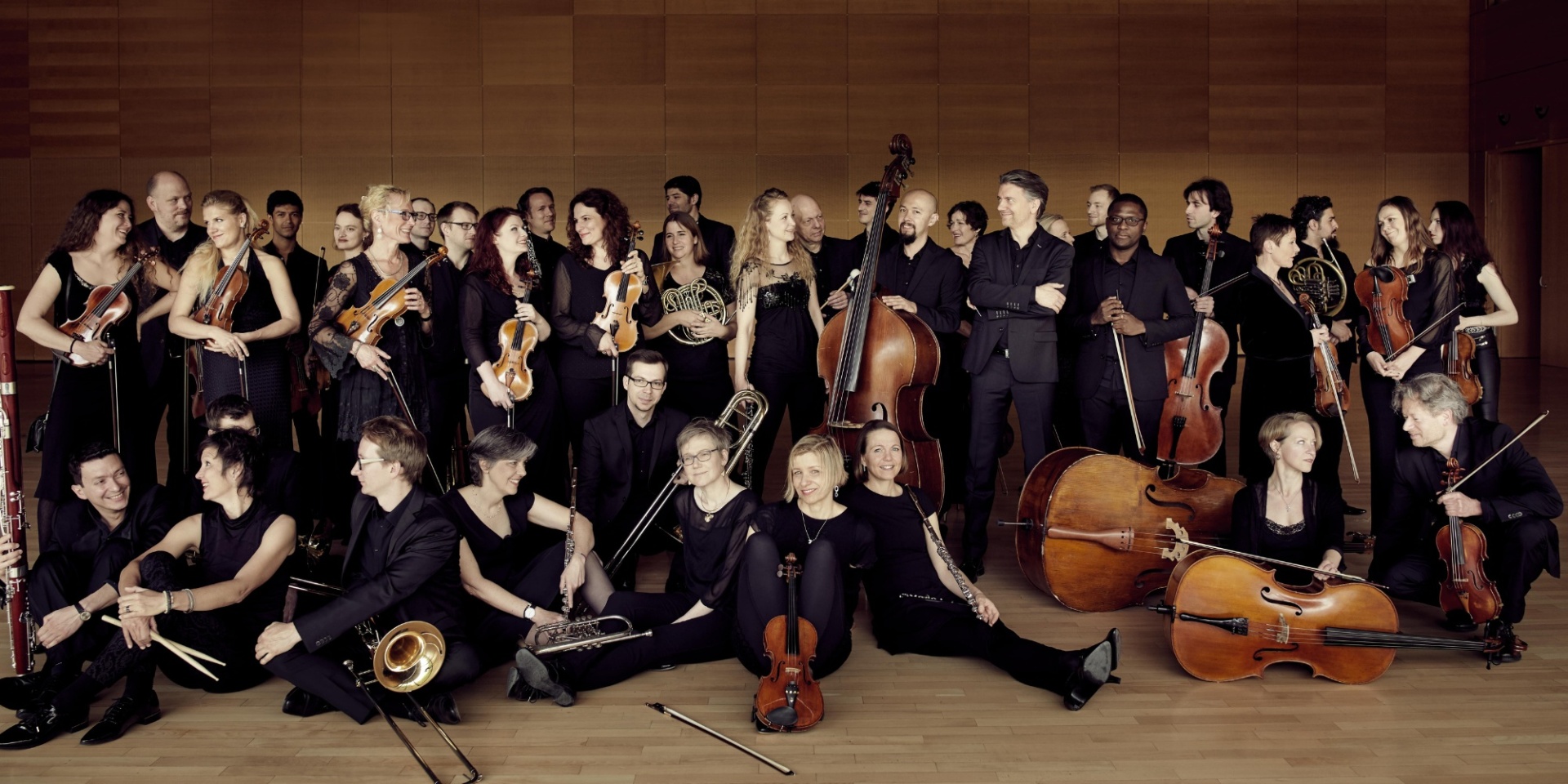 Mehrere Personen eines Orchesters mit Musikinstrumenten haltend vor einem schwarzen Hintergrund