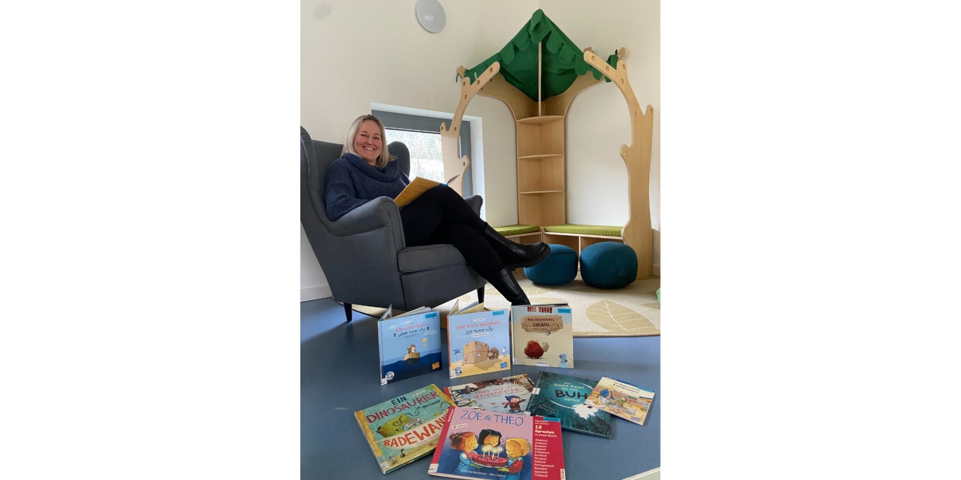 Frau sitzend in einem gemütlichen Stuhl in einer Kita. Davor sind mehrere Kinderbücher liegend auf dem Boden