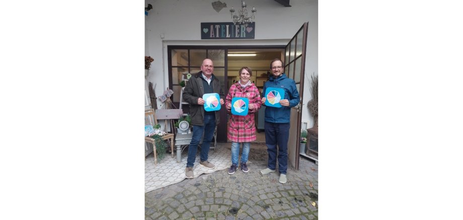 Zwei Männer und eine Frau stehen nebeneinander und halten jeweils ein Schild hoch