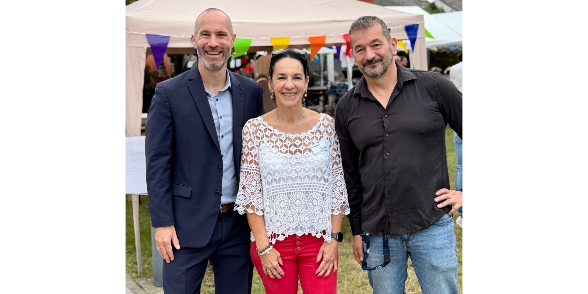 Eine Frau und zwei Männer stehend draußen. Im Hintergrund ein Zelt.