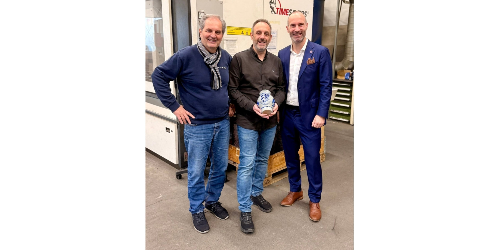 Drei Männer stehend. Der Mann in der Mitte hält einen Krug in den Händen.