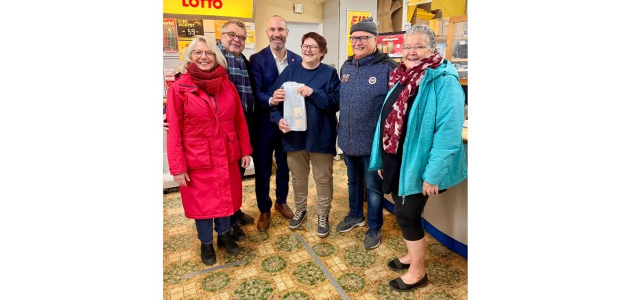 Drei Frauen und drei Männer stehend in einem Ladengeschäft.