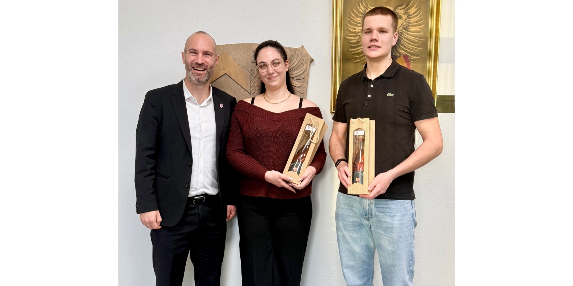 Eine Frau und zwei Männer stehend vor einer Wand.