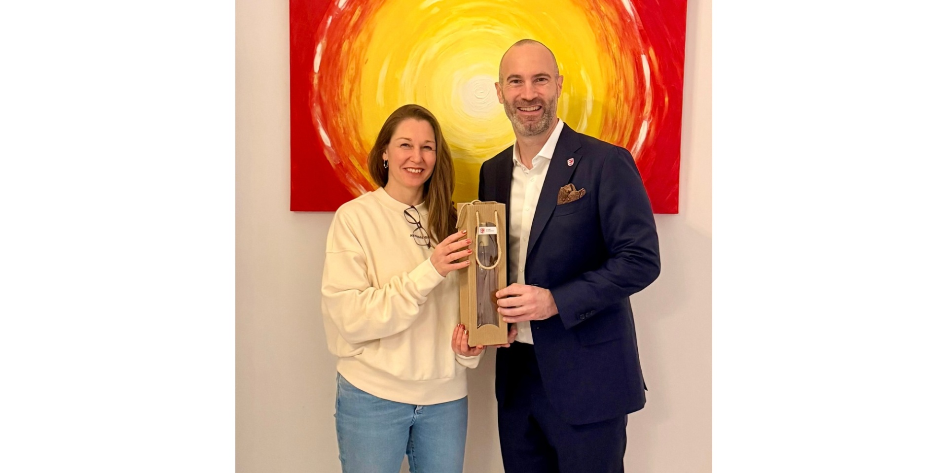 Eine Frau und ein Mann stehend und lächelnd vor einem Gemälde.