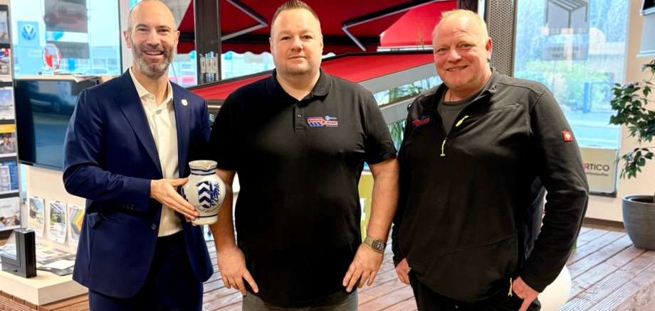 Drei Männer stehend nebeneinander. Der Mann links im Bild hält einen Apfelweinkrug in den Händen