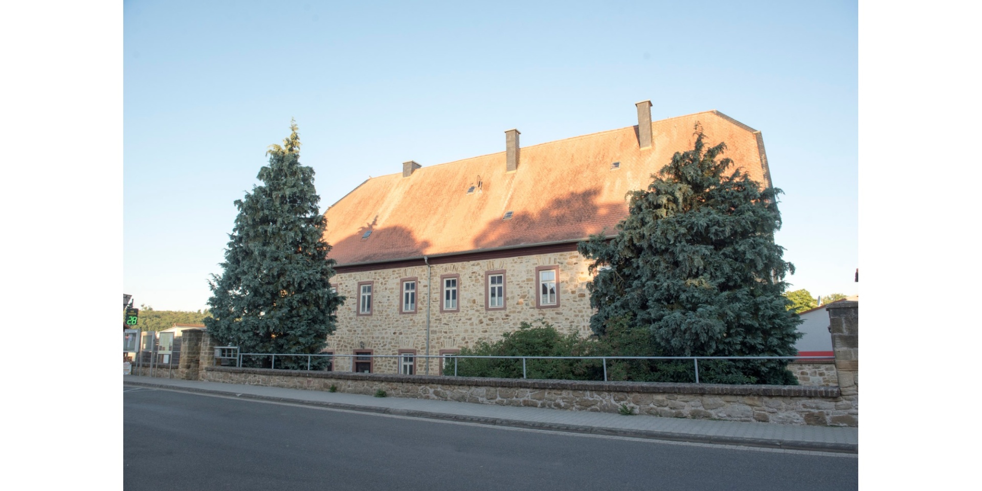Historisches Gebäude mit zwei vorgelagerten Tannenbäumen auf dem Grundstück.
