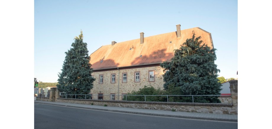 Historisches Gebäude mit zwei vorgelagerten Tannenbäumen auf dem Grundstück.