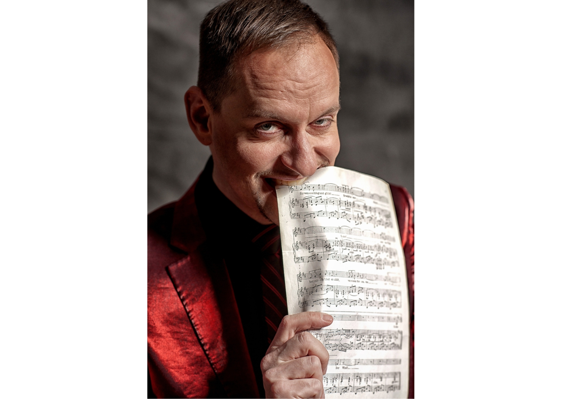 Mann in rotem Jackett beißt in ein Notenblatt