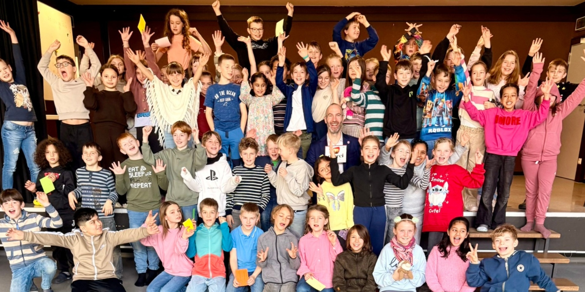 Viele Grundschulkinder jubelnd auf einem Foto. In der Mitte ein Mann lächelnd