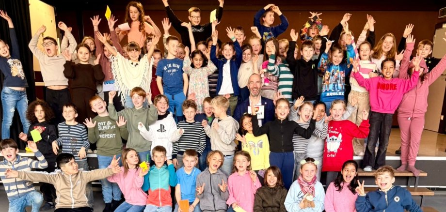Viele Grundschulkinder jubelnd auf einem Foto. In der Mitte ein Mann lächelnd