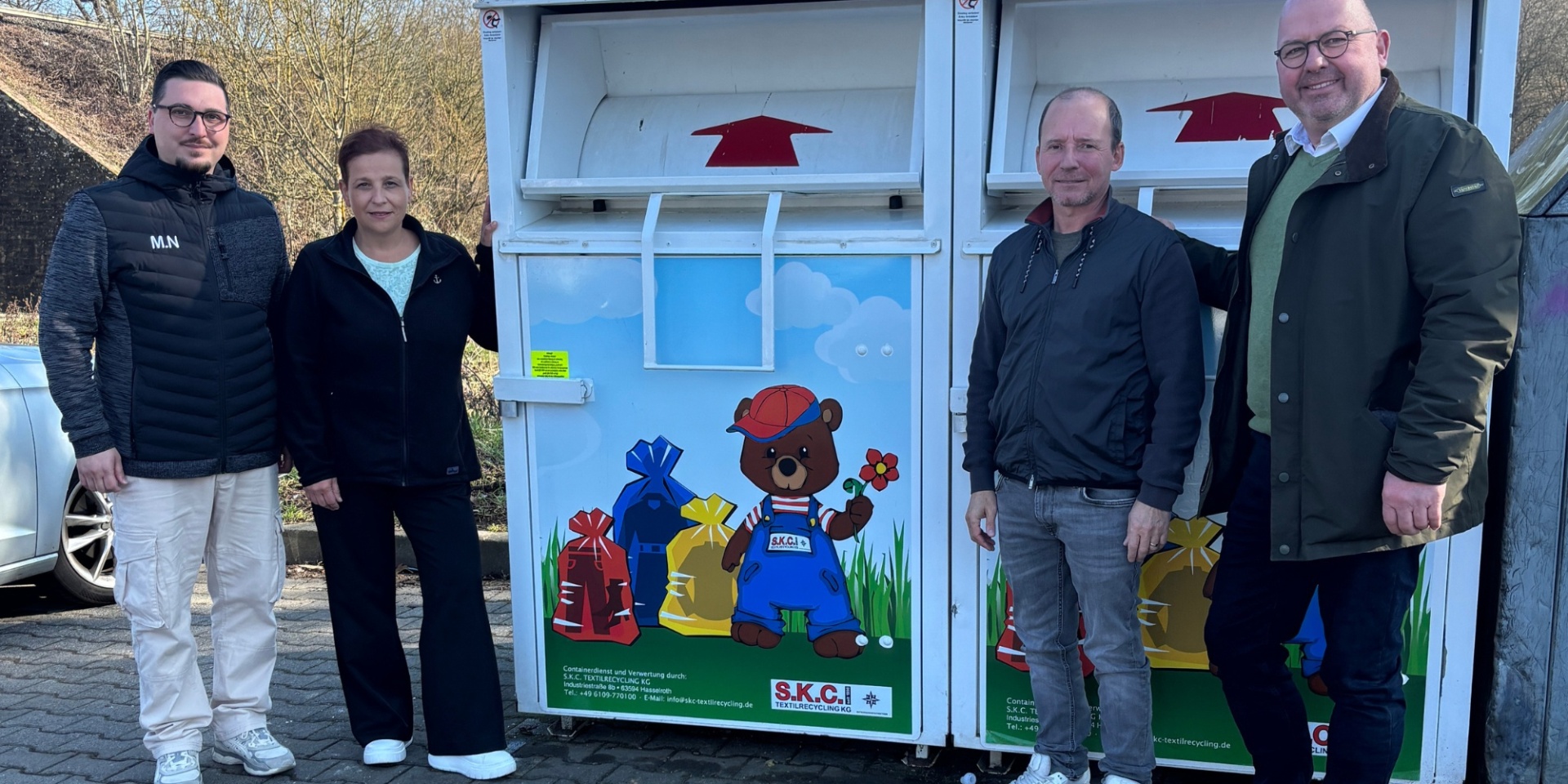 Vier Personen stehend neben Altkleidercontainern