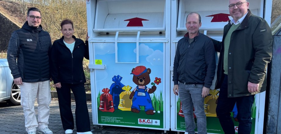 Vier Personen stehend neben Altkleidercontainern