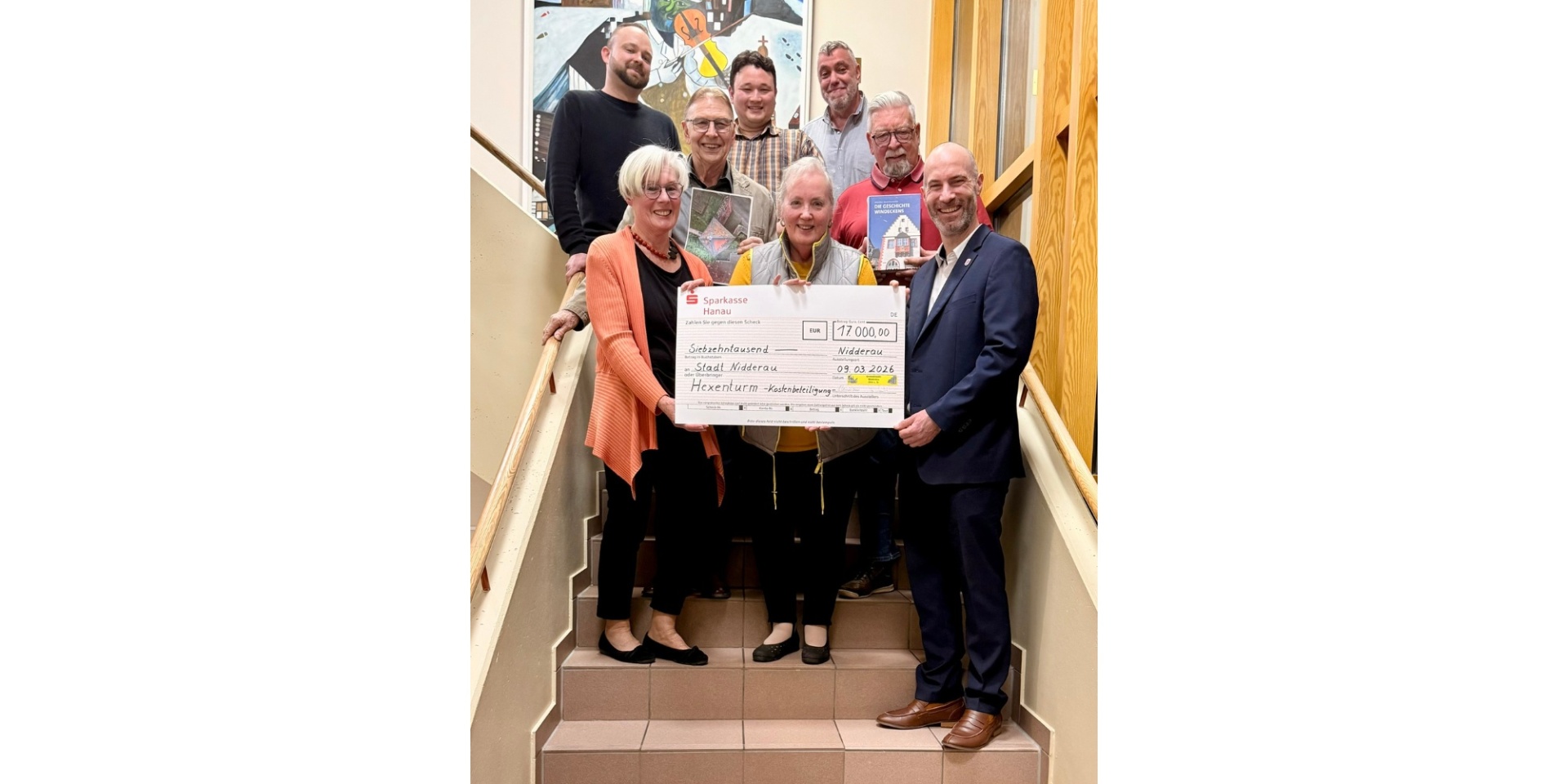 Mehrere Personen auf einer Treppe stehend, einen großen Spendenscheck haltend