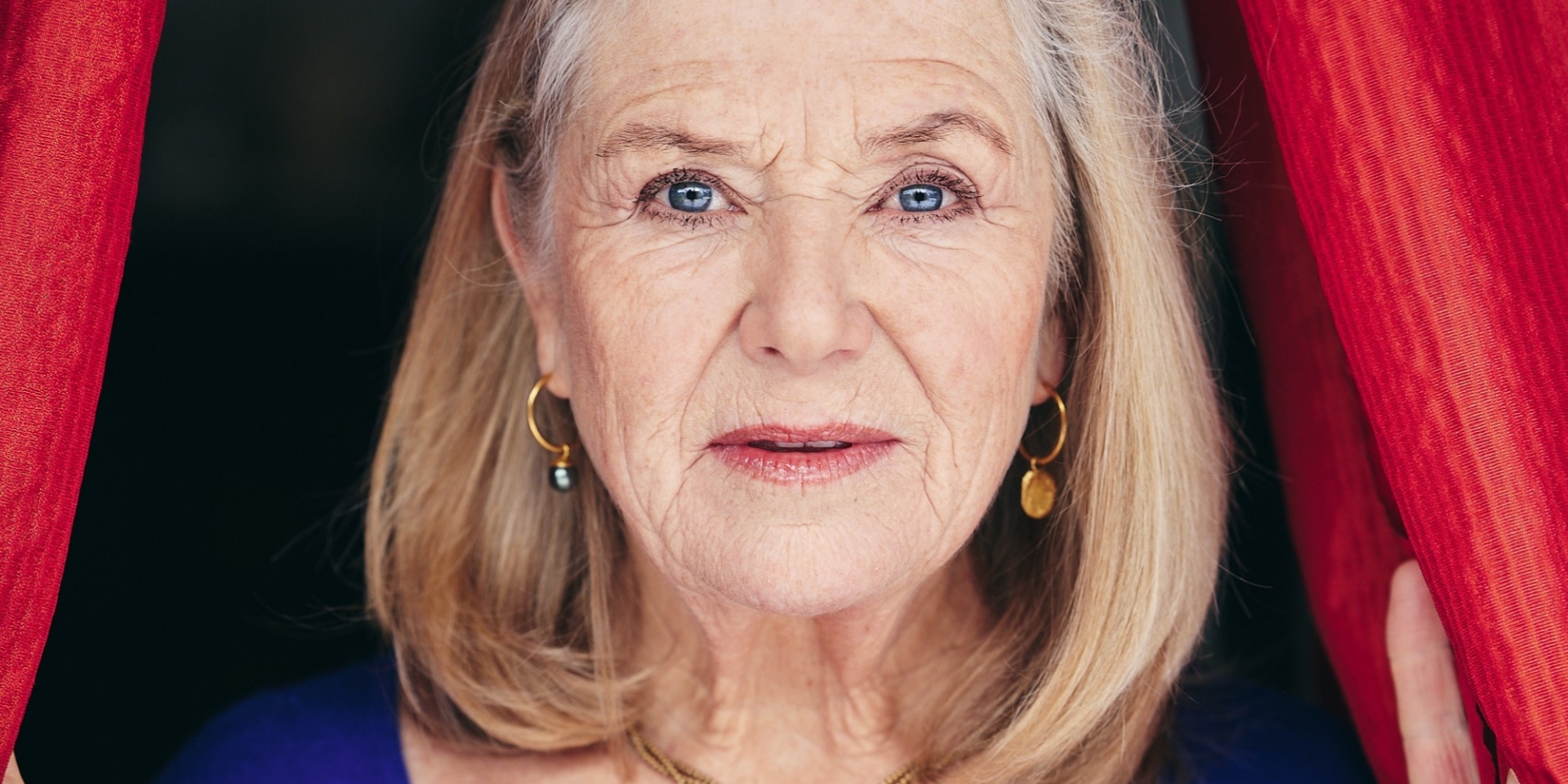 Blonde ältere Frau schaut aus einem Bühnenvorhang heraus
