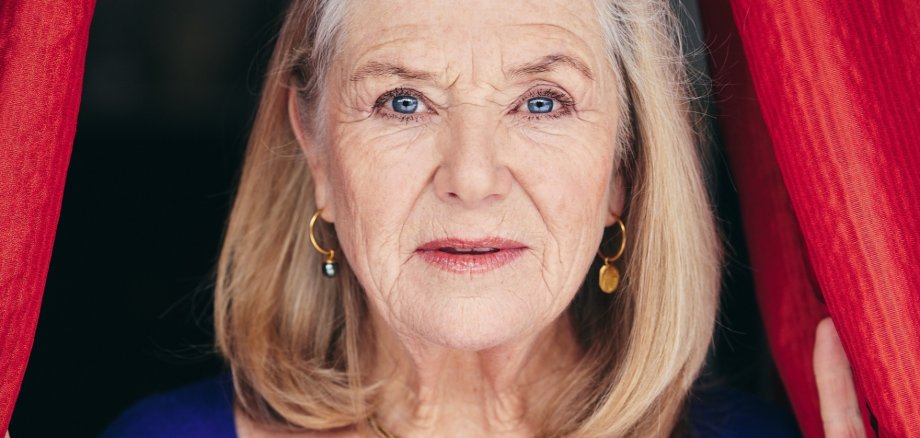 Blonde ältere Frau schaut aus einem Bühnenvorhang heraus