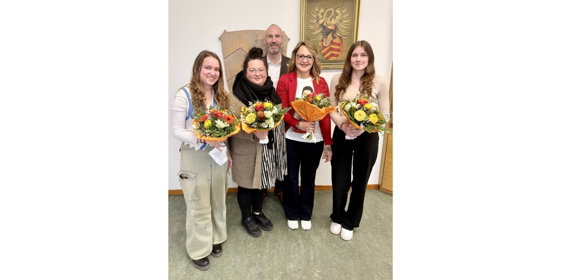 Vier Frauen mit Blumensträußen in den Händen haltend. Im Hintergrund steht ein Mann im Anzug