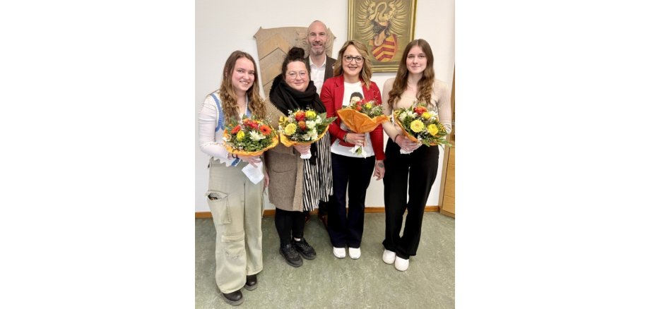 Vier Frauen mit Blumensträußen in den Händen haltend. Im Hintergrund steht ein Mann im Anzug