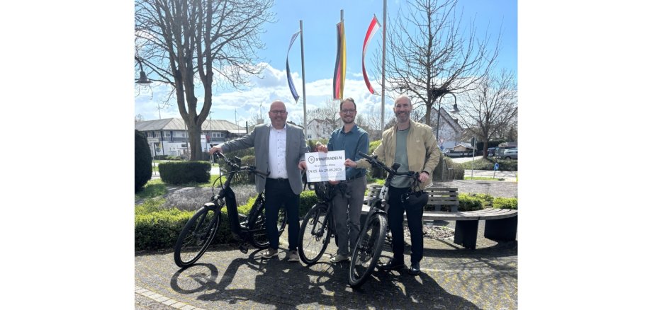 Drei Männer mit drei Fahrrädern stehend.