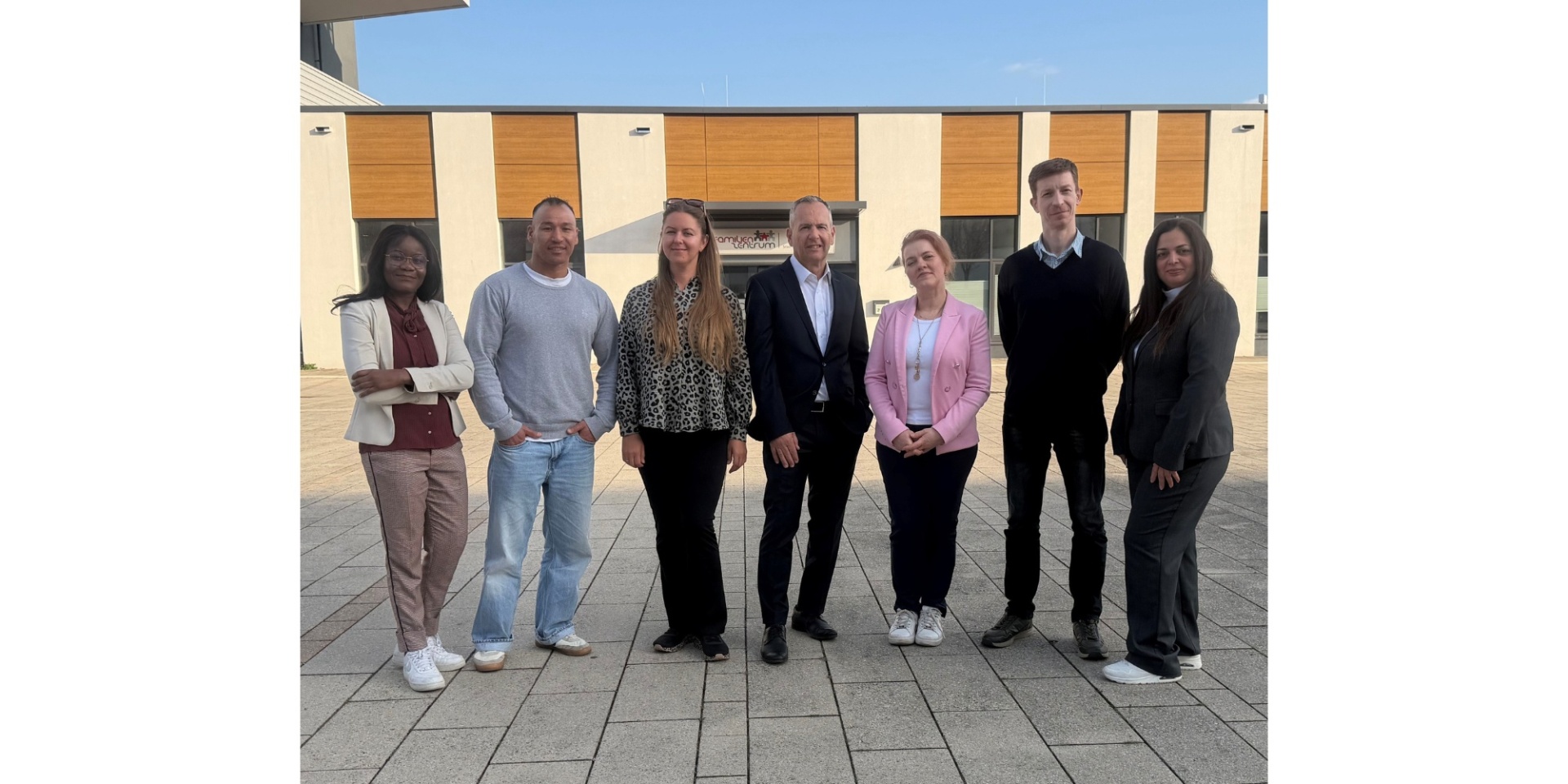 Vier Frauen und drei Männer stehend vor einem Gebäude.