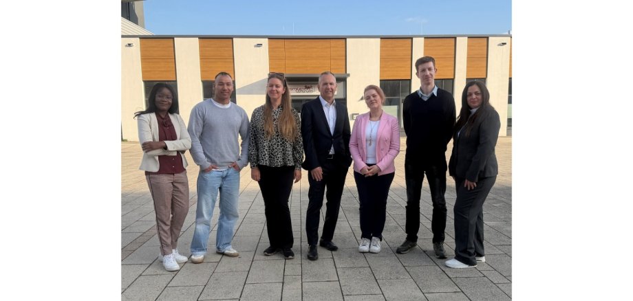 Vier Frauen und drei Männer stehend vor einem Gebäude.