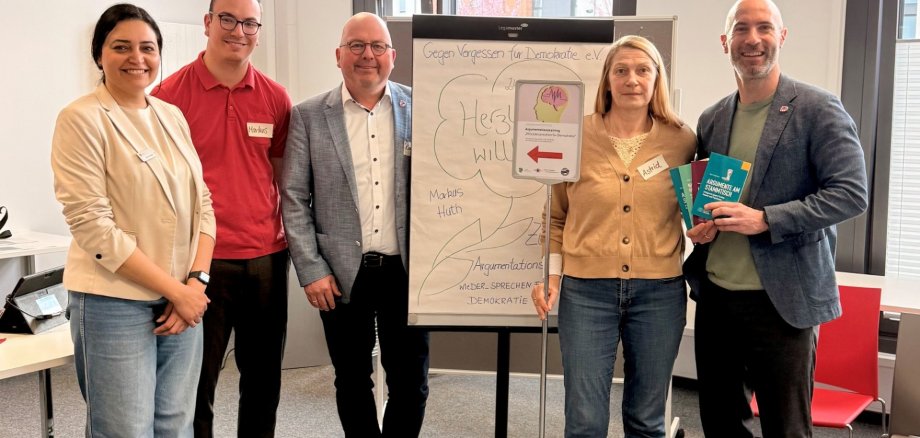 Fünf Personen stehend in einem Raum, in der Mitte ein Flipchart