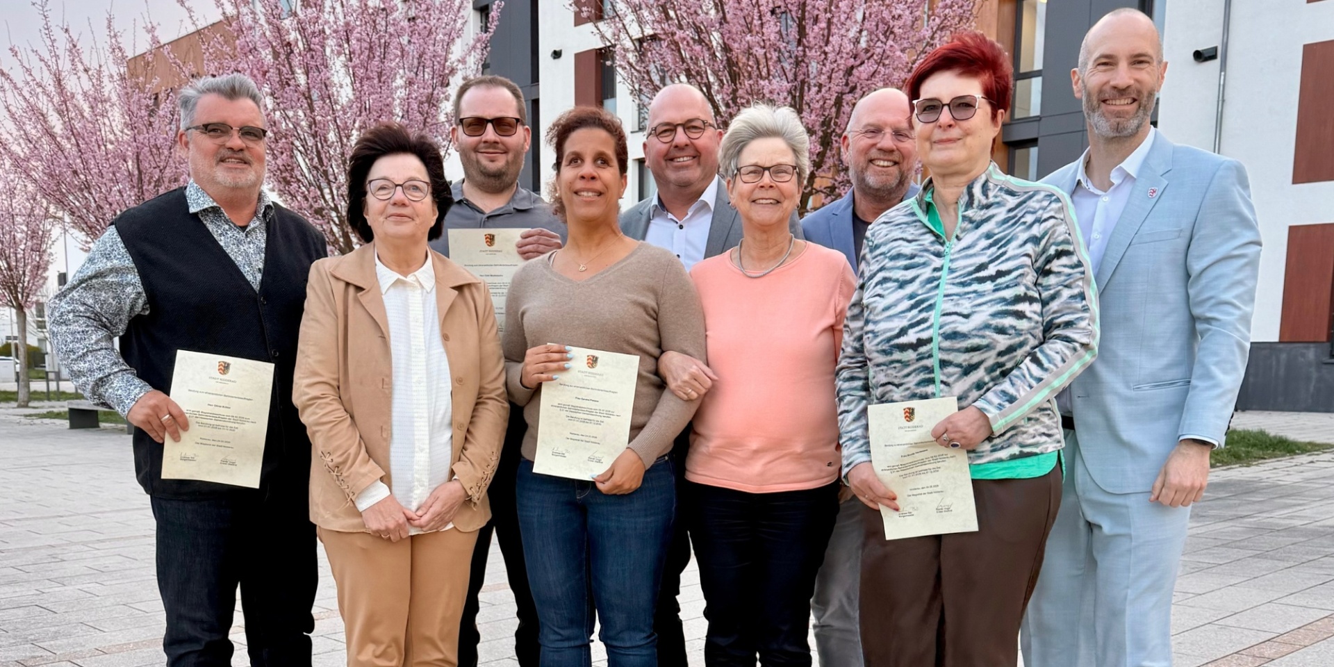 Mehrere Personen stehend auf einem Stadtplatz, ein paar von ihnen halten Urkunden in der Hand