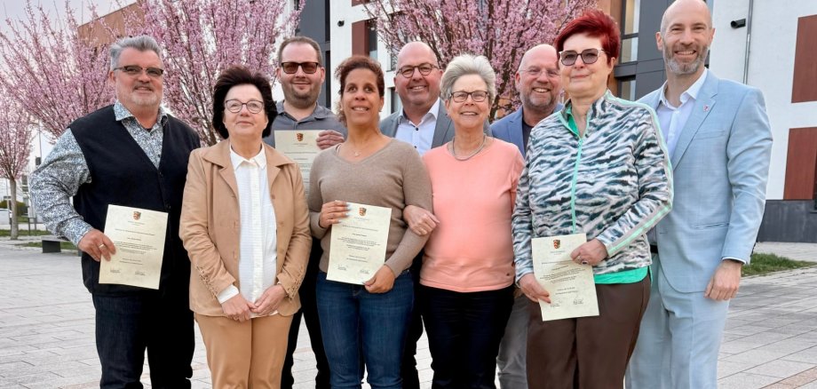Mehrere Personen stehend auf einem Stadtplatz, ein paar von ihnen halten Urkunden in der Hand
