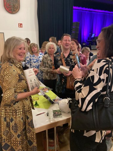 Frau signiert Bücher umringt von Leuten