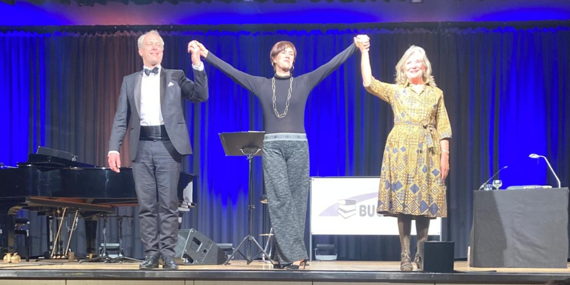 Zwei Frauen und ein Mann reichen sich die Hände auf einer Bühne