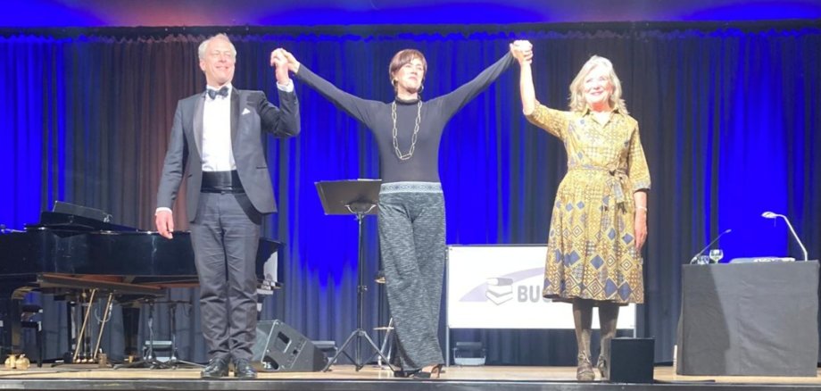 Zwei Frauen und ein Mann reichen sich die Hände auf einer Bühne