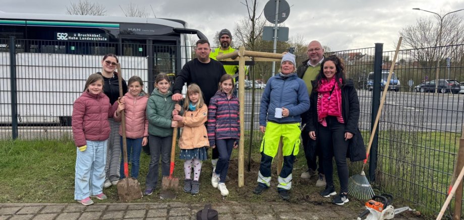 Mehrere Kinder stehen neben einem neu gepflanzten Baum