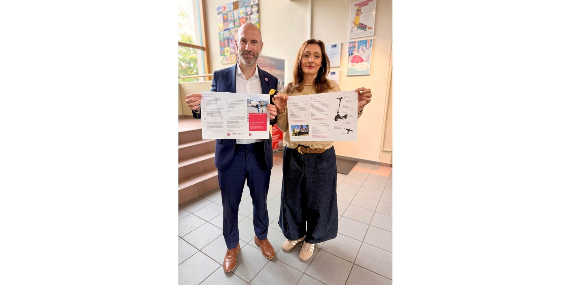 Ein Mann und eine Frau halten jeweils ein Plakat zu E-Scootern in den Händen