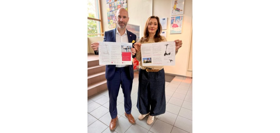 Ein Mann und eine Frau halten jeweils ein Plakat zu E-Scootern in den Händen