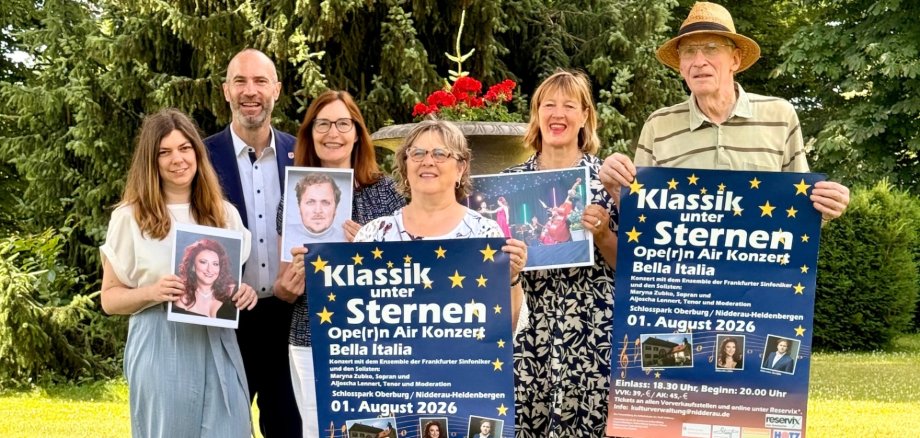 Vier Frauen und zwei Männer stehen nebeneinander in einem Park. Jeder hält entweder ein Veranstaltungsplakat oder ein Bild eines Künstlers in der Hand