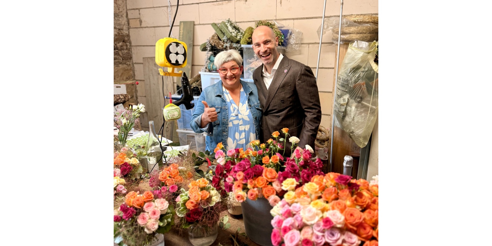 Eine Frau und eine Mann stehend. Im Vordergrund Blumensträuße.