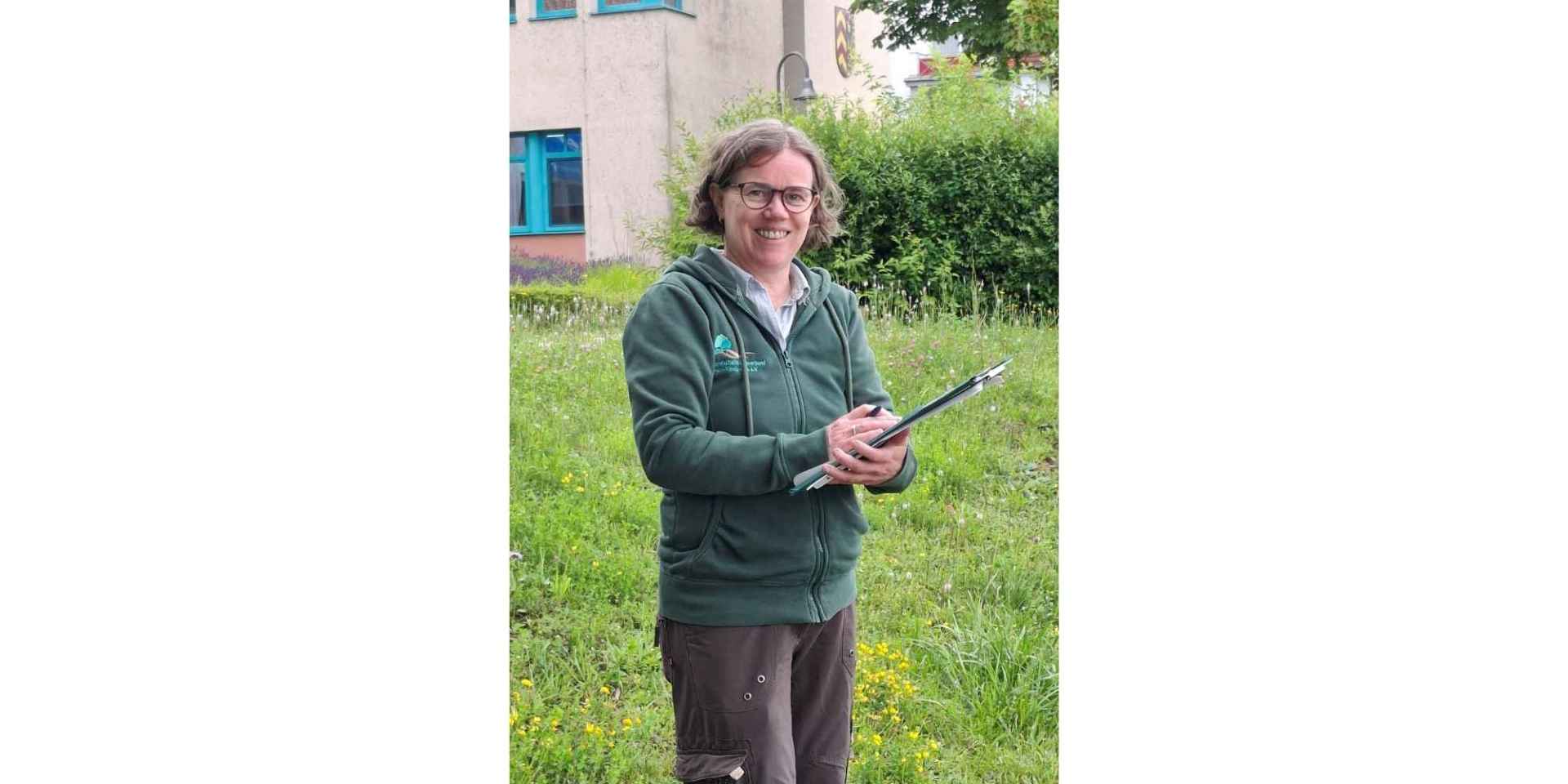 Frau mit Brille stehend vor einem Gebäude mit einem Klemmbrett in der Hand