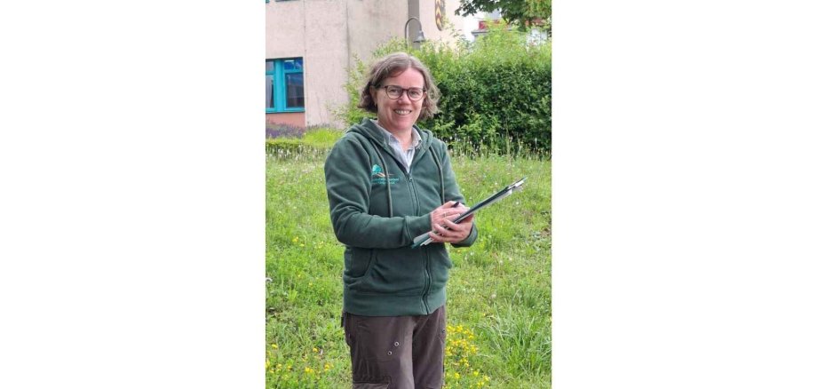 Frau mit Brille stehend vor einem Gebäude mit einem Klemmbrett in der Hand