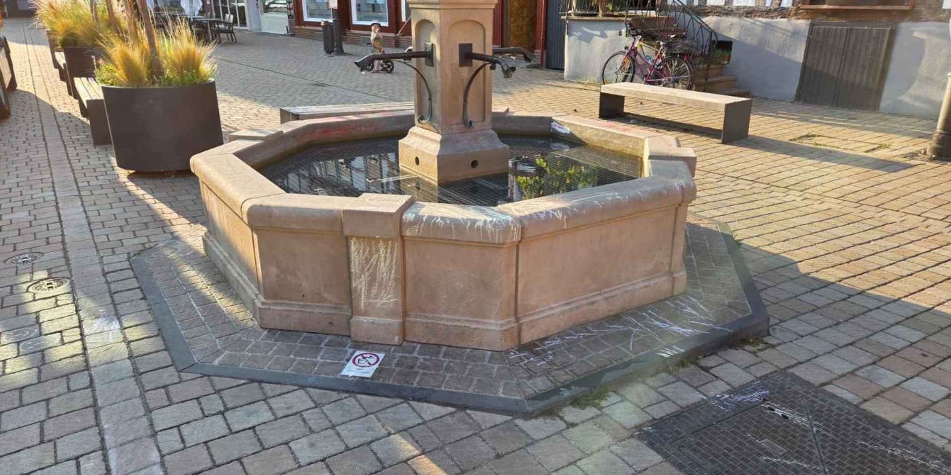 Brunnen aus Sandstein mit Schmierereien aus Kreide auf einem Marktplatz
