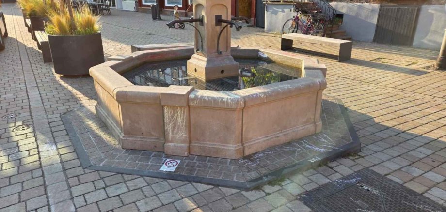 Brunnen aus Sandstein mit Schmierereien aus Kreide auf einem Marktplatz