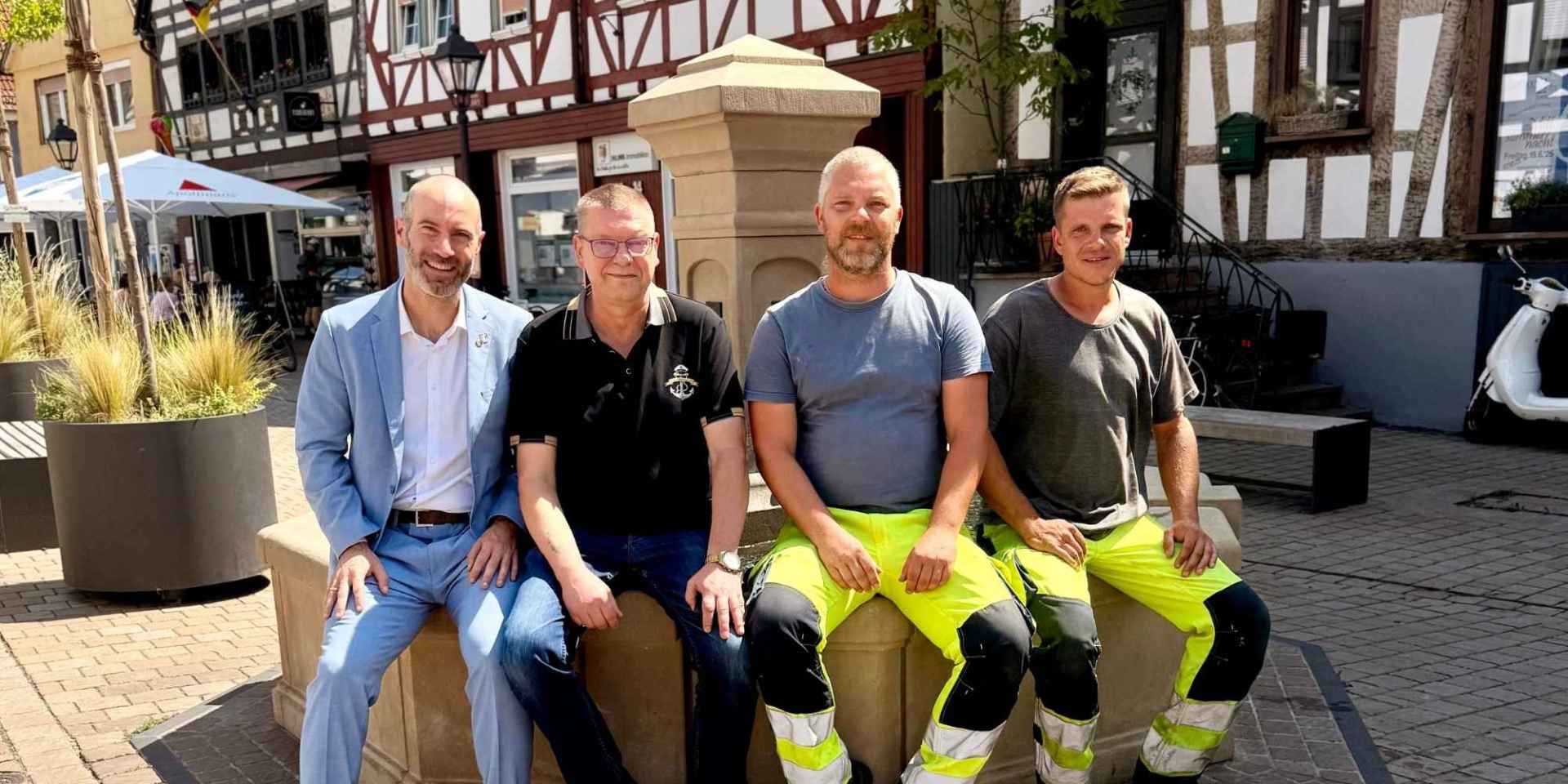 Mehrere Männer sitzend auf dem Rand eines Brunnens auf einem Marktplatz