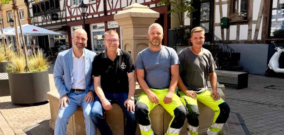 Mehrere Männer sitzend auf dem Rand eines Brunnens auf einem Marktplatz
