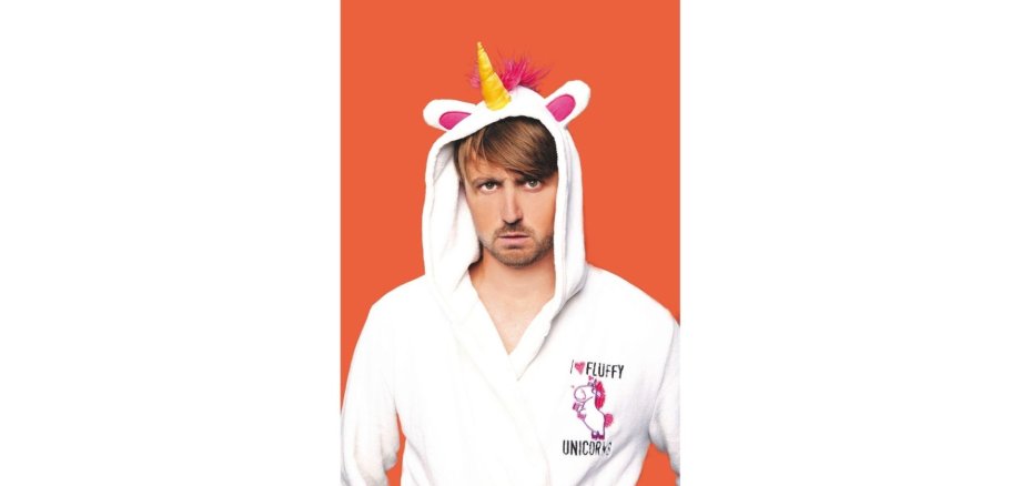Mann in einem Einhorn-Kostüm vor orange-farbenem Hintergrund