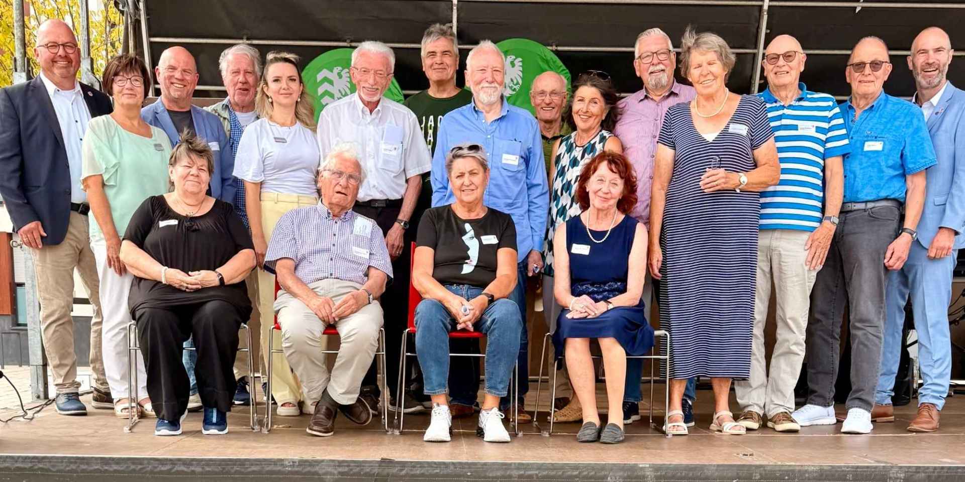 Mehrere Senioren auf einer Bühne im Freien sitzend oder stehend