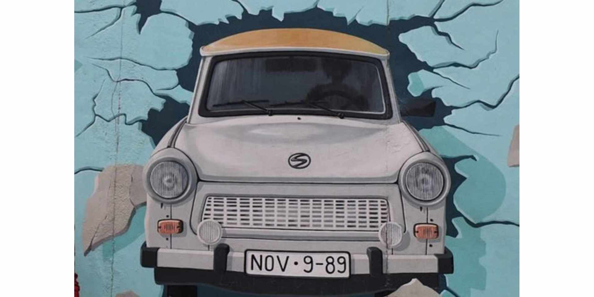Bild an der Berliner Mauer: Grauer Trabbi durchbricht eine blaue Wand
