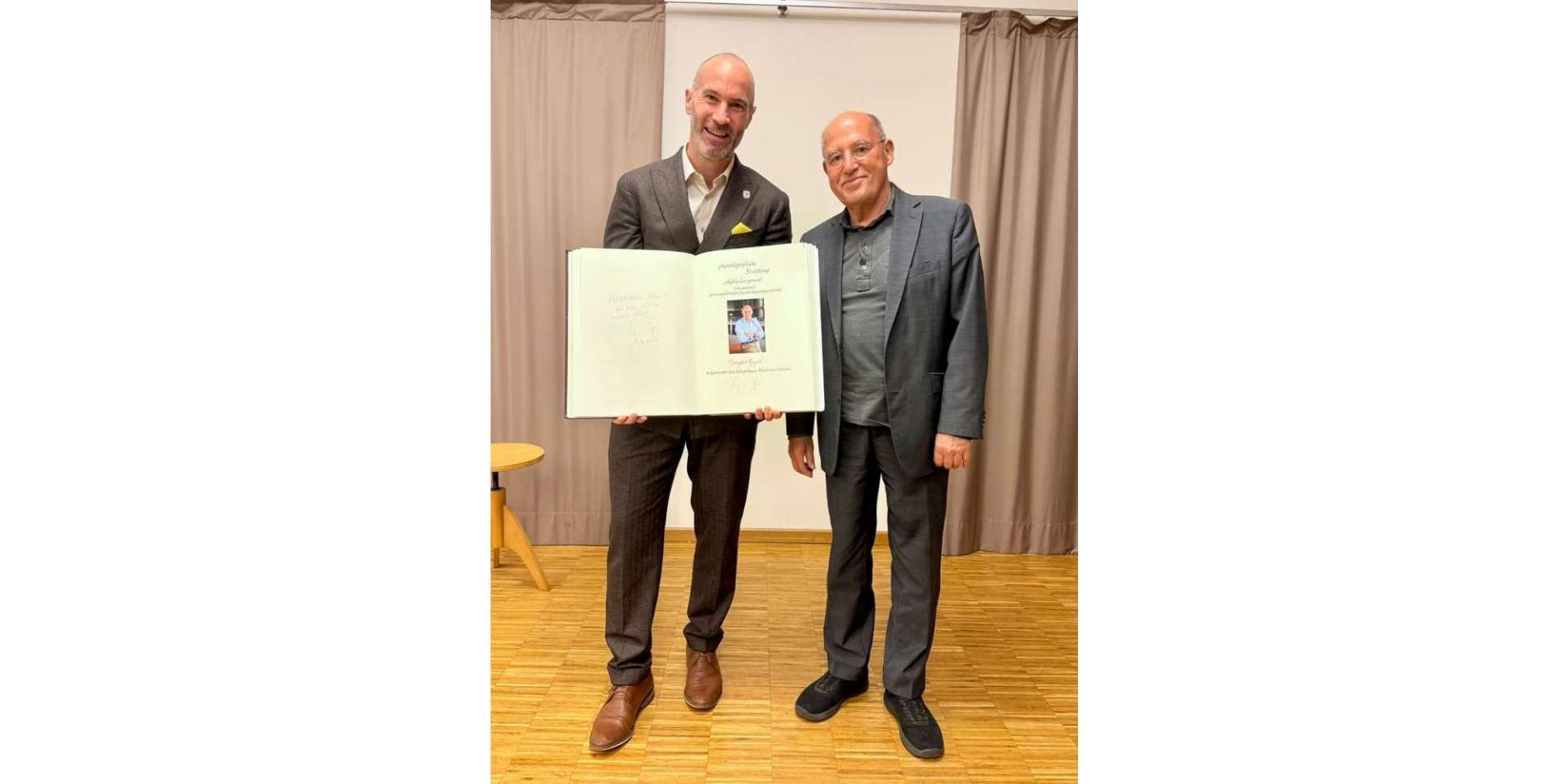 Zwei Männer in Anzügen stehend nebeneinander. Ein Mann hält ein geöffnetes Buch vor sich