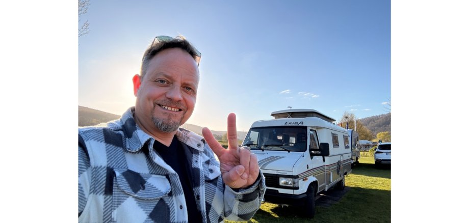 Mann lächelnd im karierten Hemd, vor einem Wohnmobil