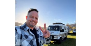 Mann lächelnd im karierten Hemd, vor einem Wohnmobil