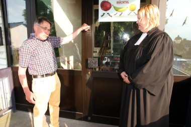 Mann schließt eine Tür eines Gebäudes. Daneben steht eine Pfarrerin