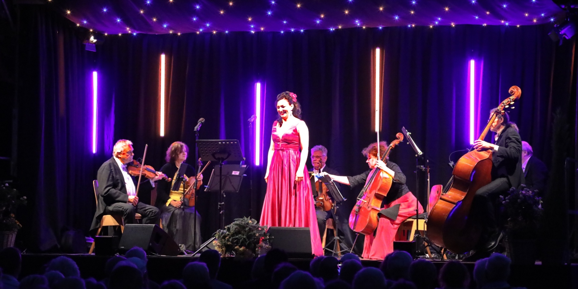 Dame in rotem Abendkleid stehend auf einer Bühne umgeben von Musikern